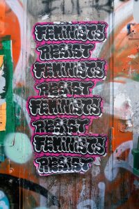 En betongvägg med graffiti med klistermärken med texten feminists resist som upprepas